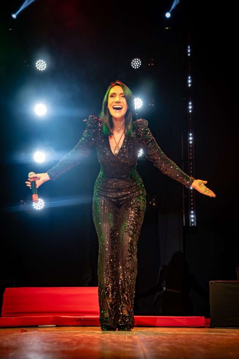 Rebeca Aldana de cuerpo entero en el escenario, brazos abiertos