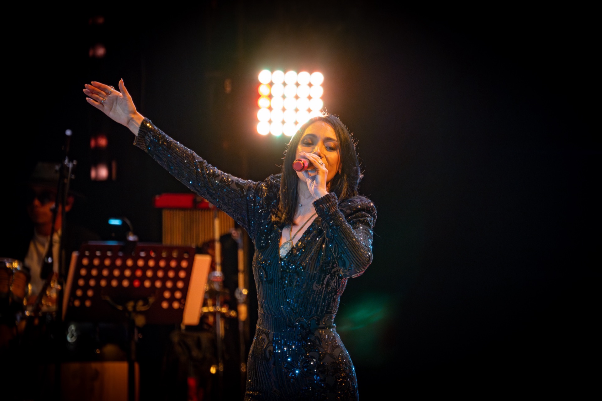 Rebeca Aldana cantando con el brazo en alto, acompañada por su orquesta