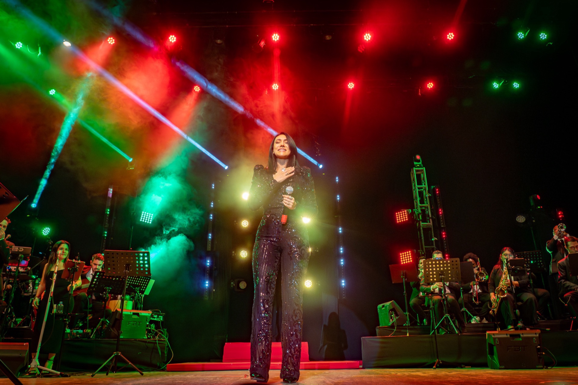 Rebeca Aldana en el escenario del Teatro Armando Manzanero con la Mérida Big Band, bajo luces rojas y verdes